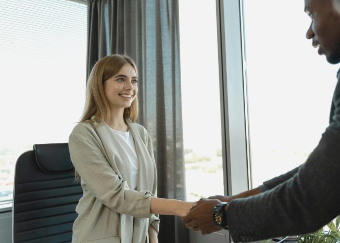 pexels-photo-5439153-5439153 Woman smiling and shaking hands at a business office, signaling a successful job interview.